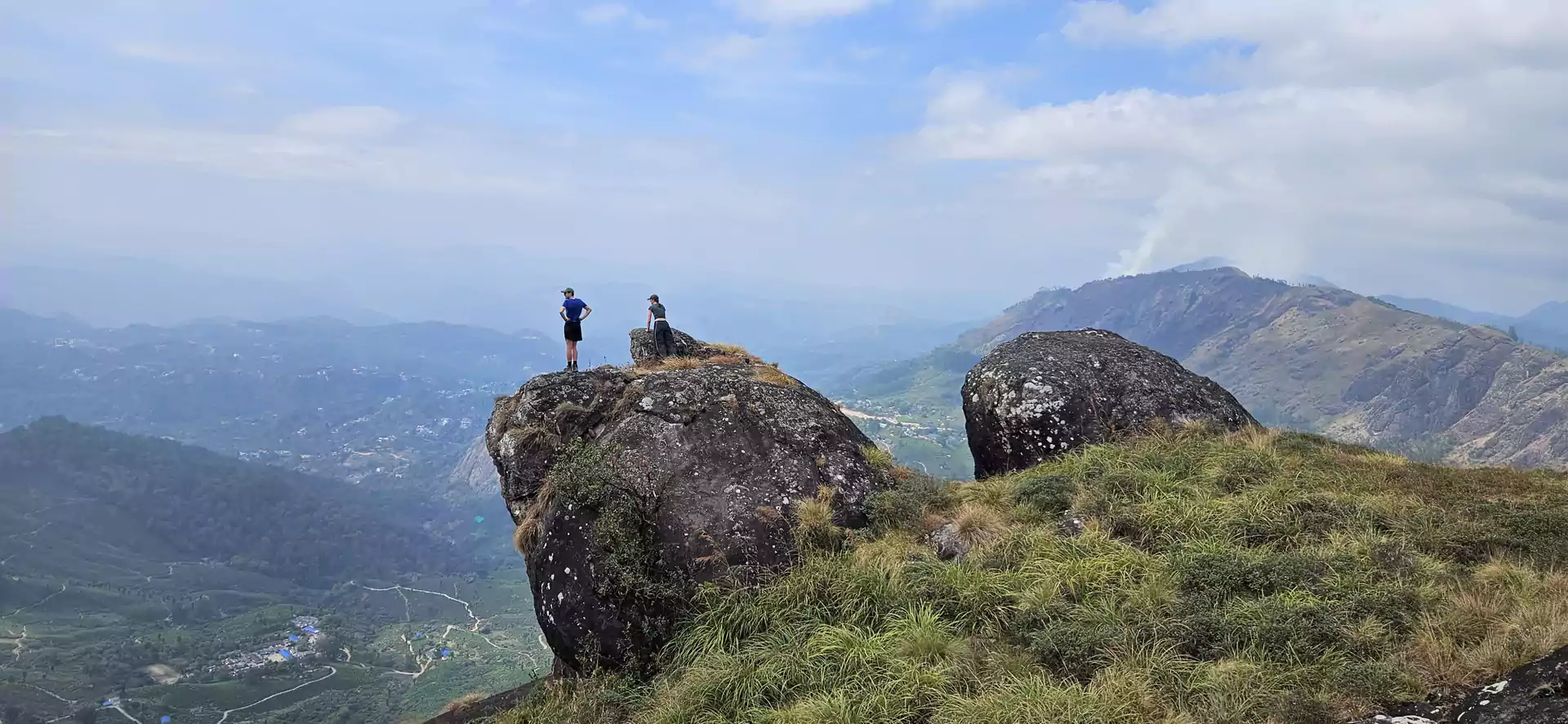 Couple enjoying a panoramic mountain view during a trekking adventure in Munnar, overlooking the rolling hills and lush landscapes of the Western Ghats.