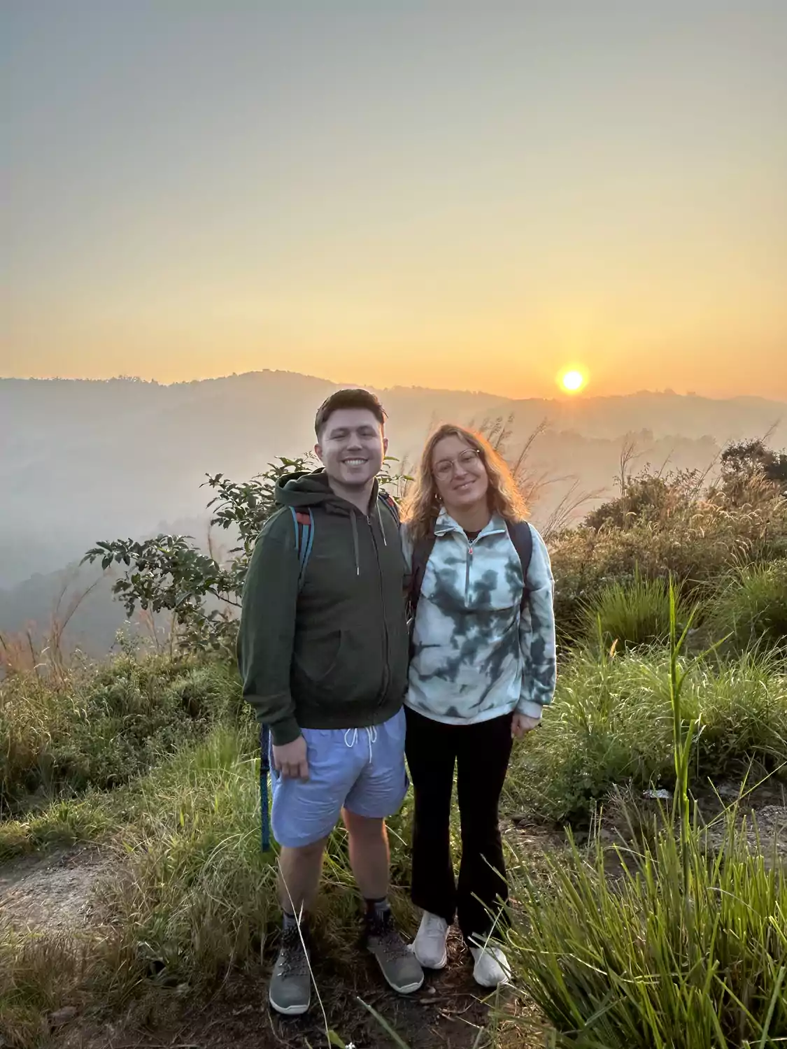 Couple enjoying a spectacular sunrise over the Western Ghats from Nadukani Viewpoint during an early morning jeep journey near Munnar.